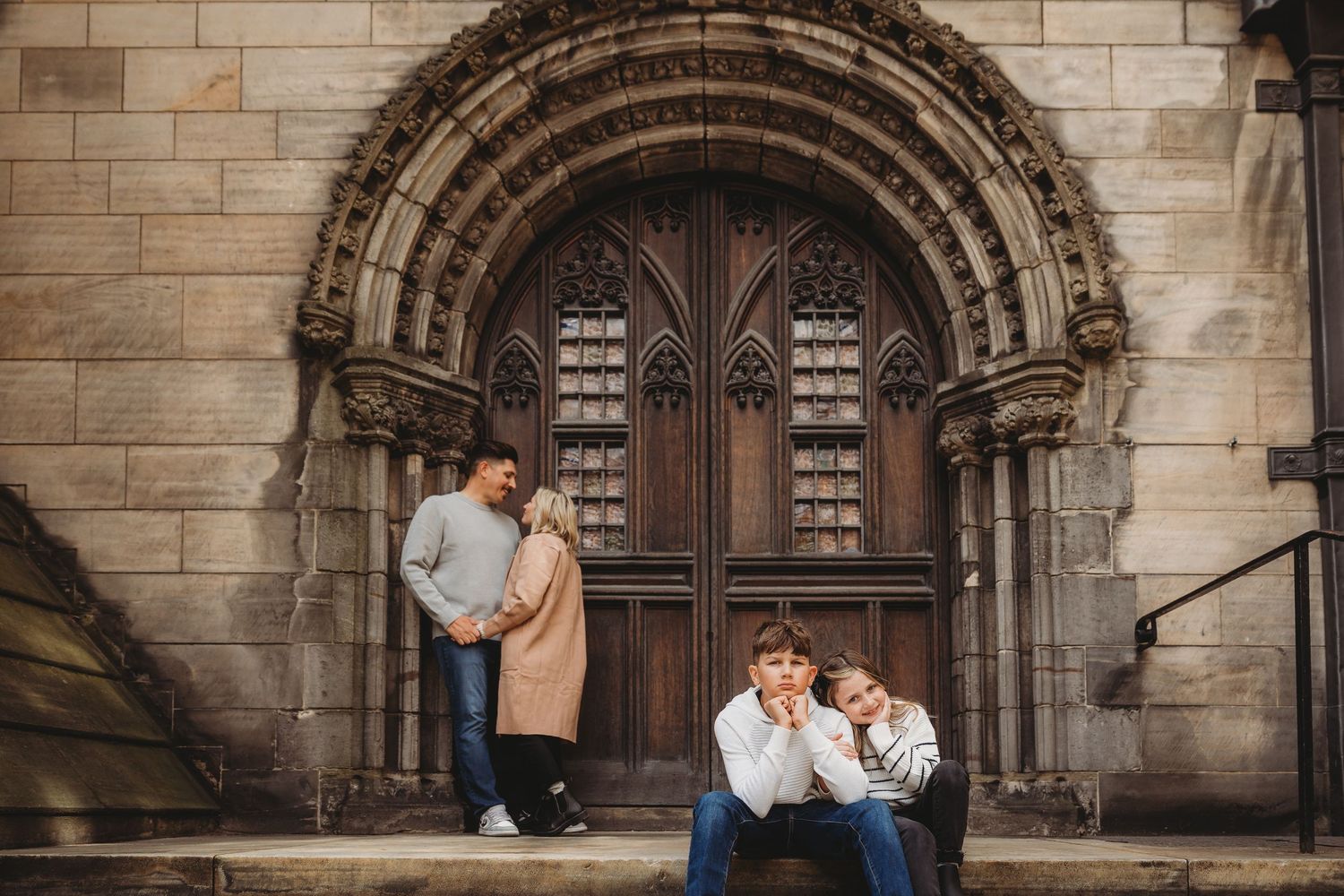 Family portrait session in front of ornate church doors with Romanesque architecture and stone archway.