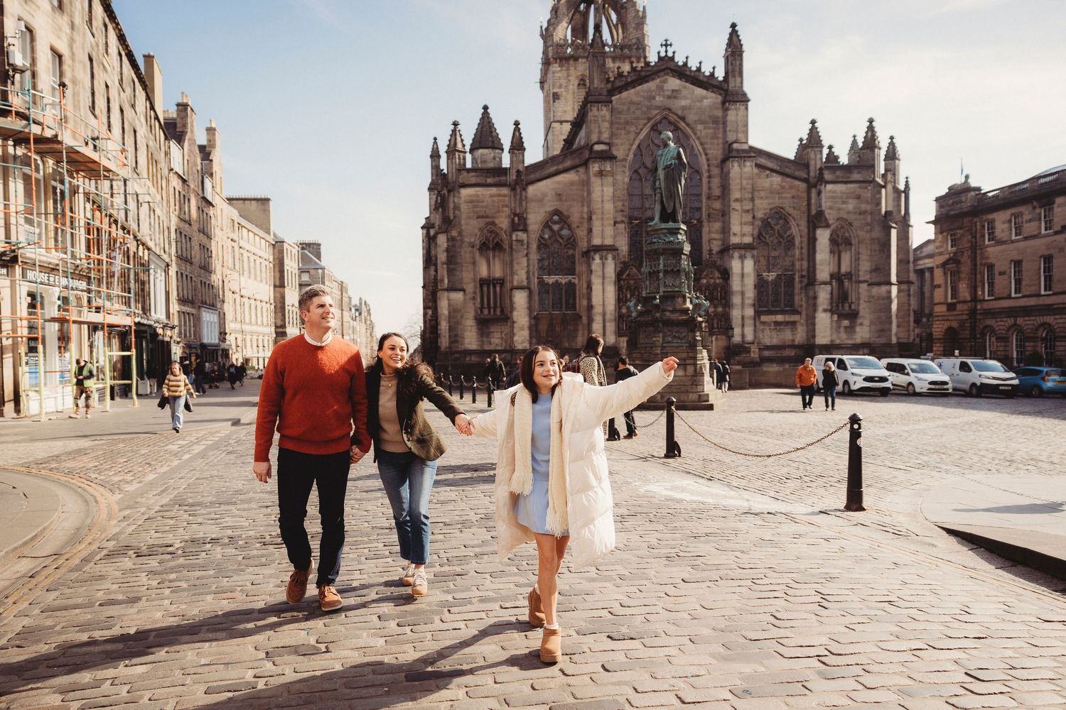 Three friends walking on Royal Mile cobblestones with St Giles Cathedral in Edinburgh, Scotland background.