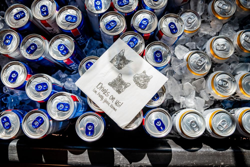 Assorted beverage cans chilled on ice with a decorative wedding drink sign at a reception bar.