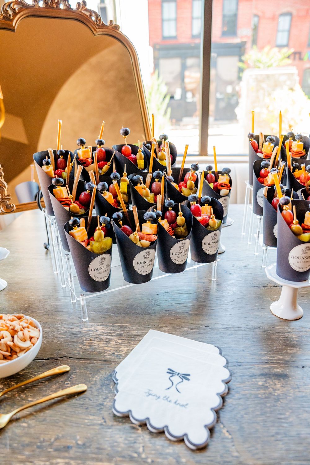 Elegant wedding reception fruit skewer appetizers displayed in black cones on a wooden table with custom napkins.