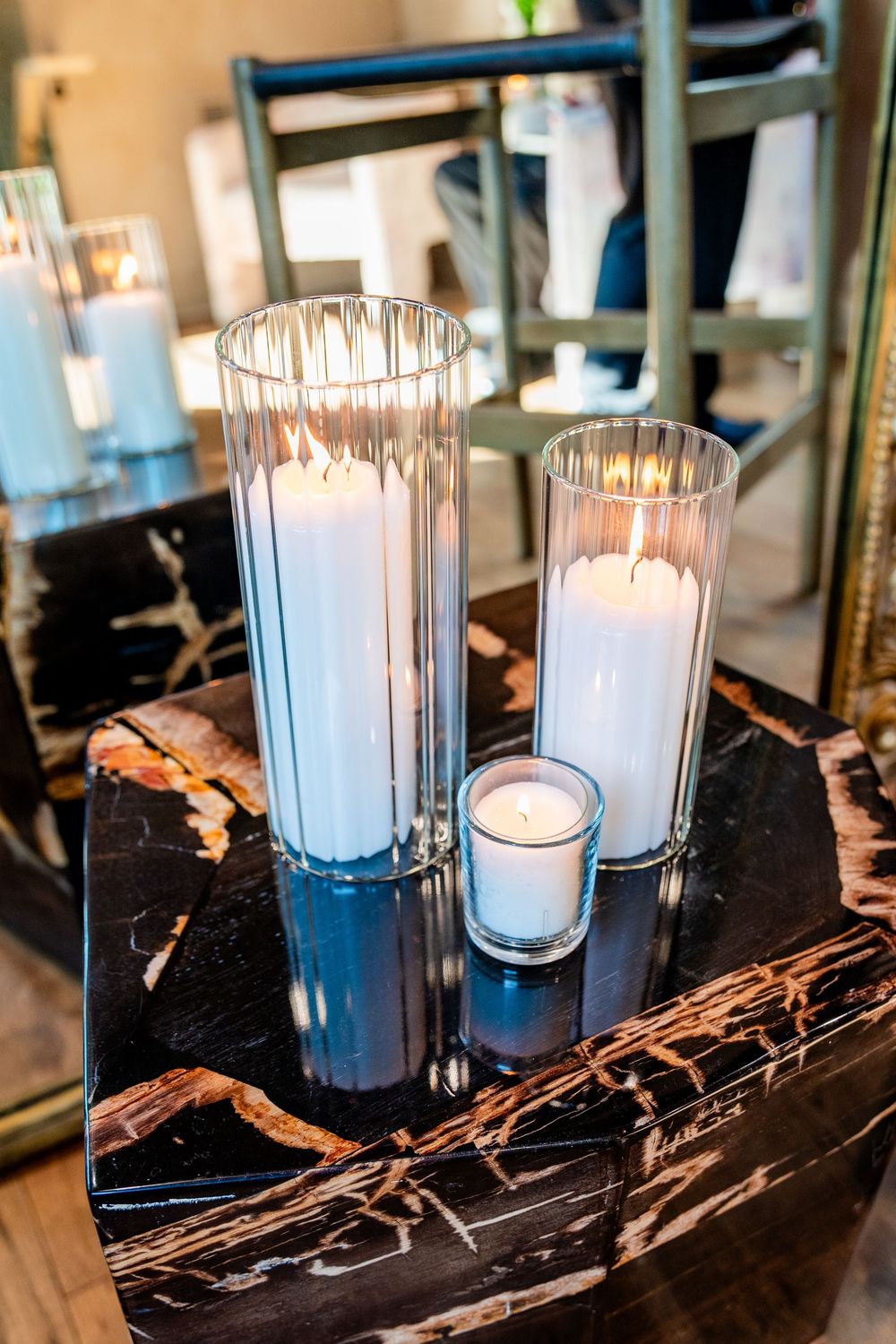 Three white pillar candles in glass hurricane holders displayed on a black marble surface at a wedding.