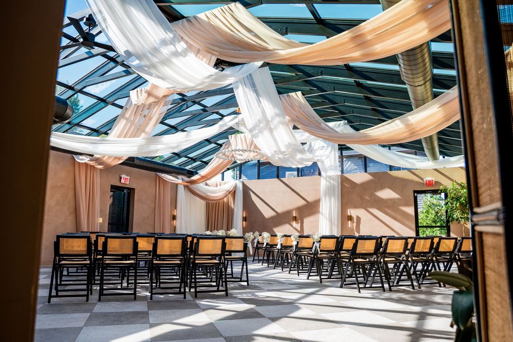 Elegant wedding ceremony venue with draped fabric ceiling, black chairs, and a glass skylight roof.