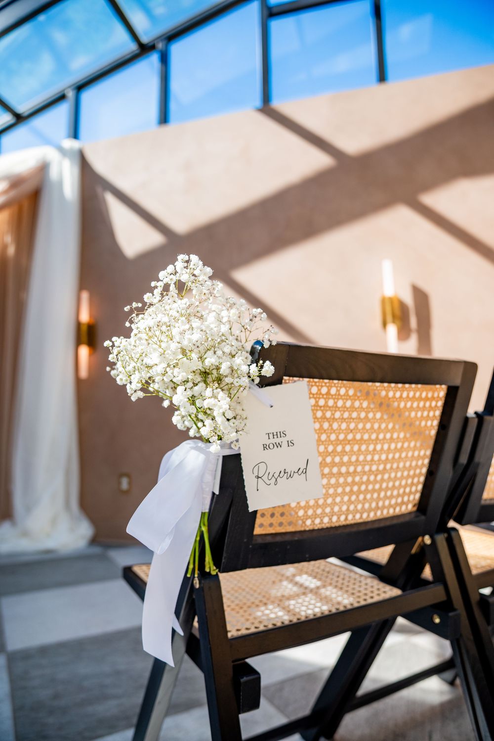 A reserved row chair decorated with white baby's breath flowers and a white ribbon bow at a wedding ceremony.