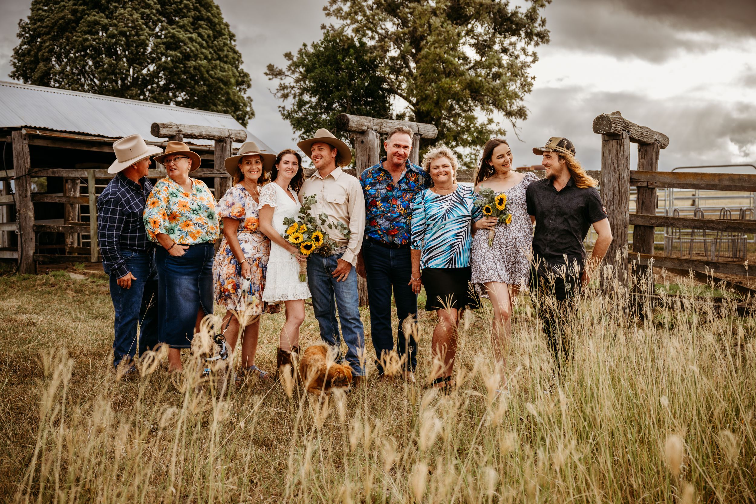 Large family group posing together in a rustic field near a wooden fence, wearing colorful western outfits.