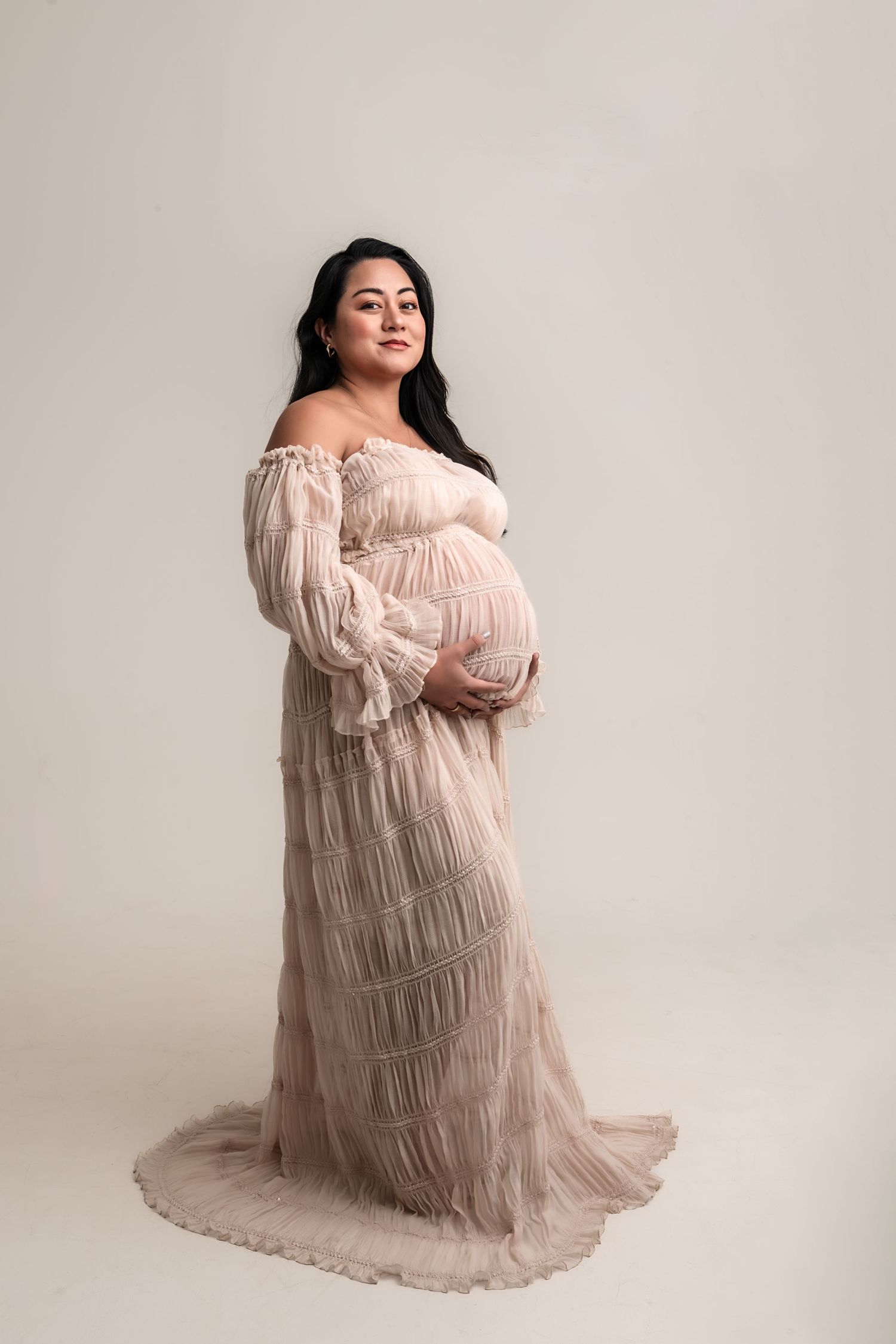 Pregnant woman in elegant off-shoulder blush tulle maternity gown in professional studio portrait by Atlanta maternity photographer.