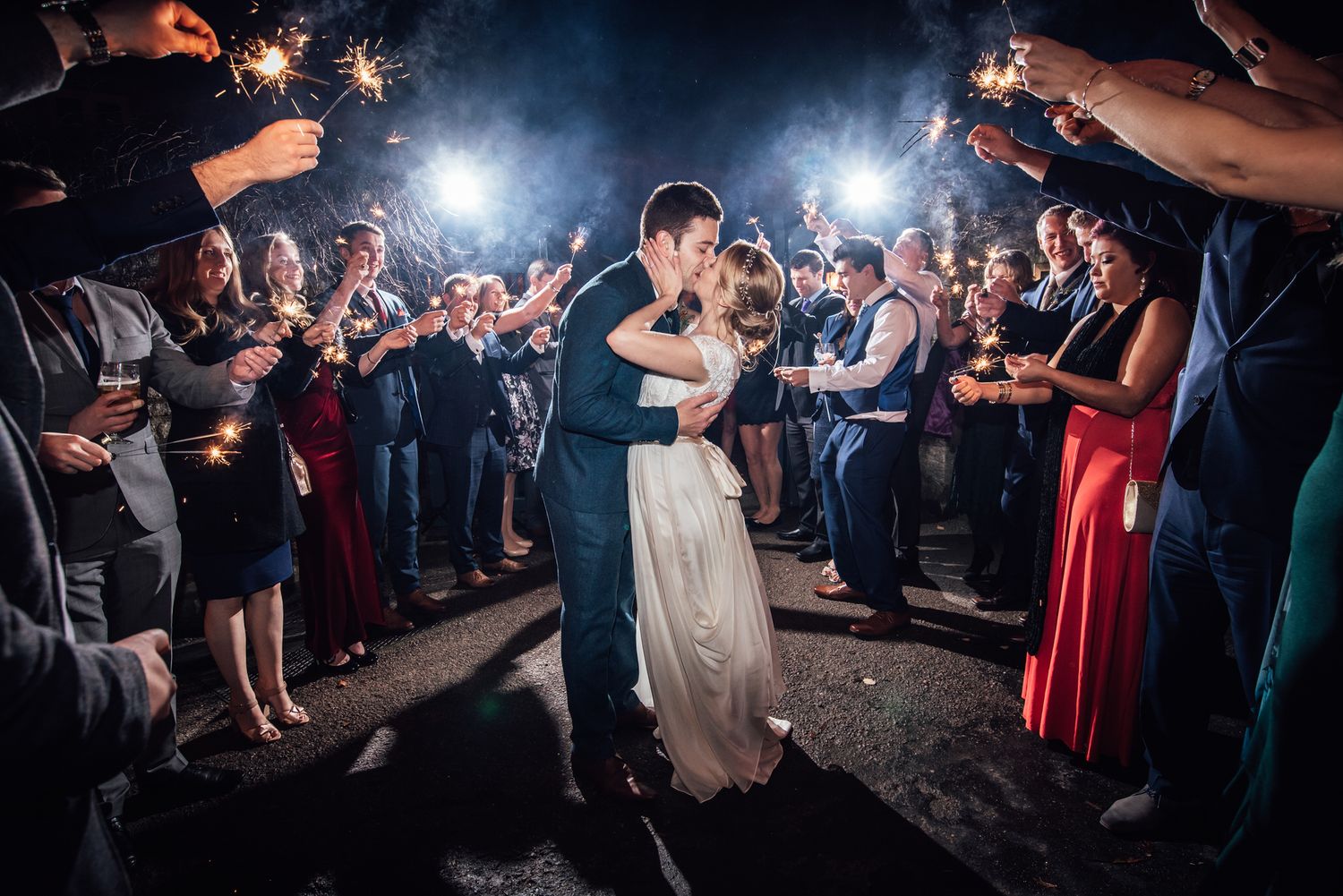 Bride and groom share a kiss surrounded by guests holding sparklers at their Swan Bibury Wedding Venue