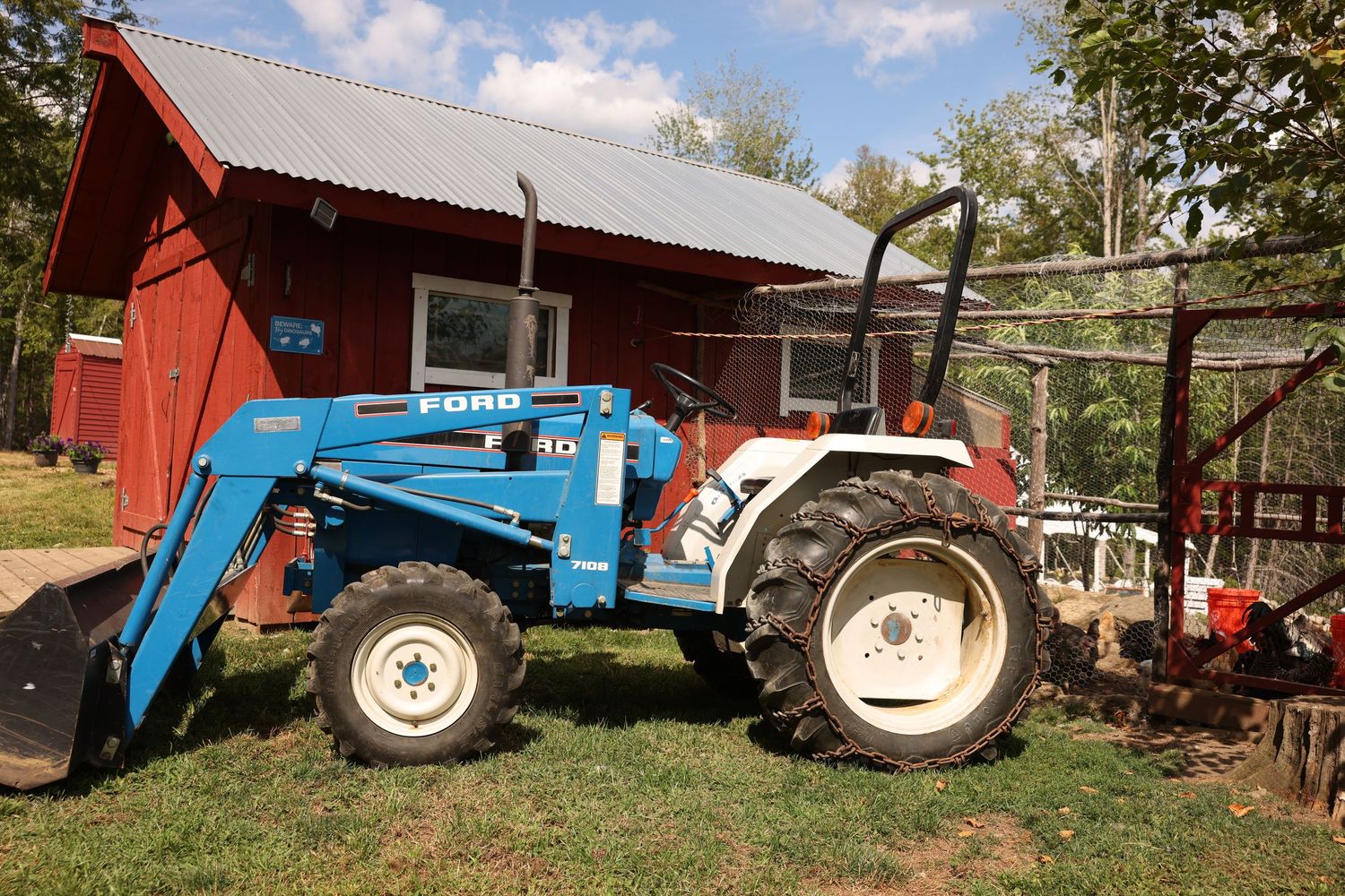 Blue and white Ford tractor with front loader parked outside a red barn on a sunny day.
