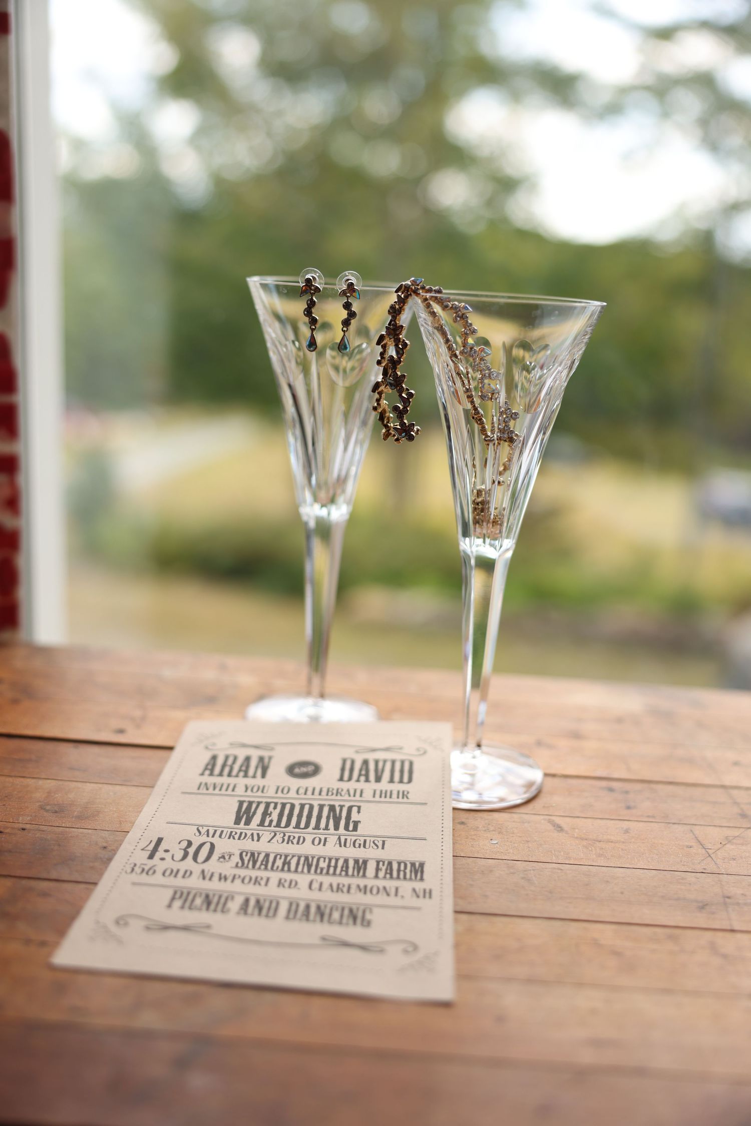 Crystal champagne flutes with wedding invitation for Aran and David at Snackingham Farm on wooden table.