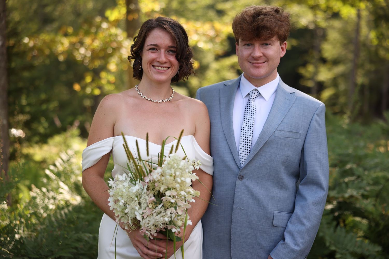 Smiling bride and groom posing together outdoors in lush green forest wedding setting.
