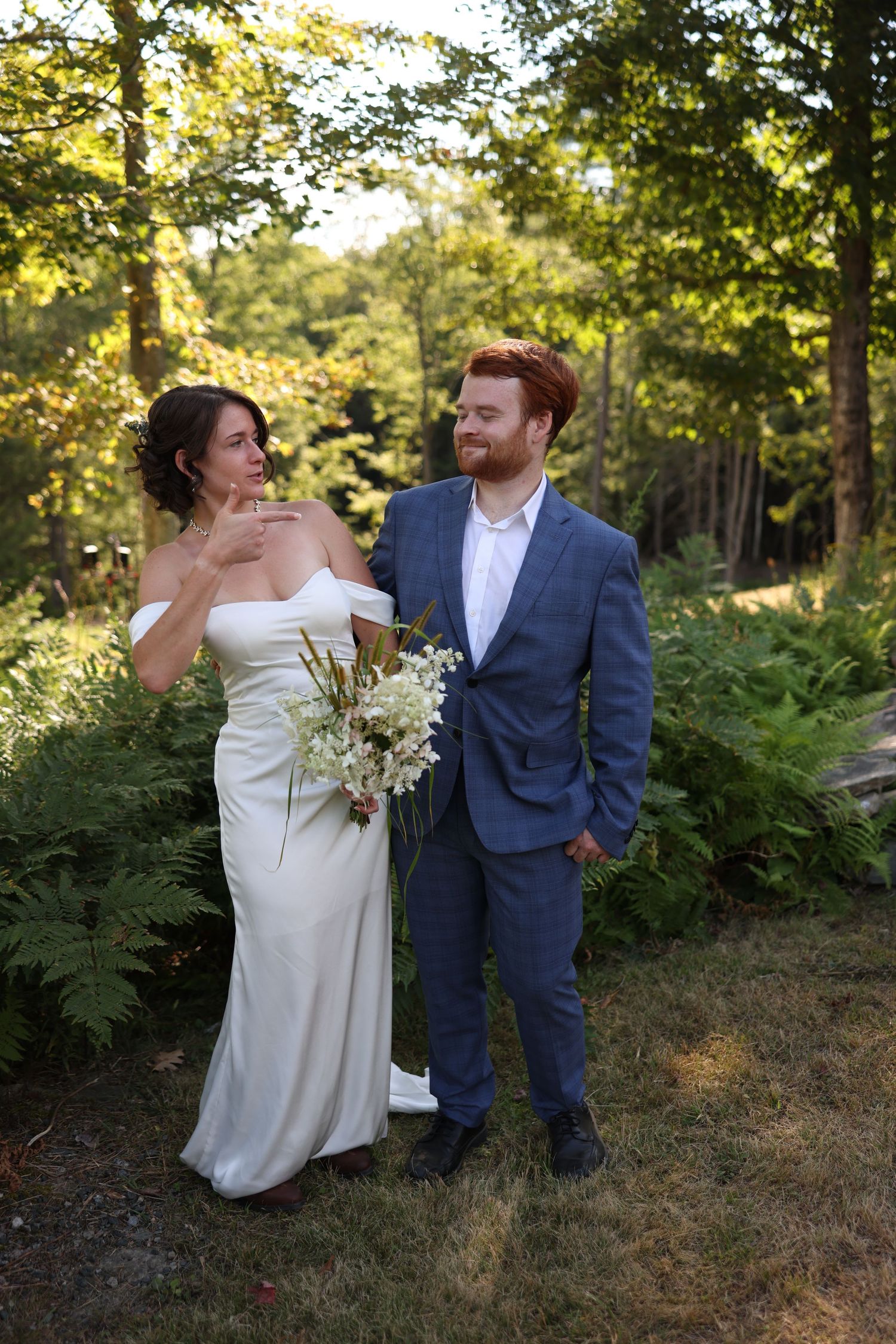 Bride and groom standing together in sunlit garden surrounded by ferns at wedding.