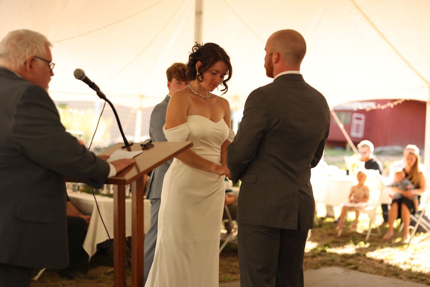Bride and groom holding hands during wedding vows ceremony under white tent outdoors.