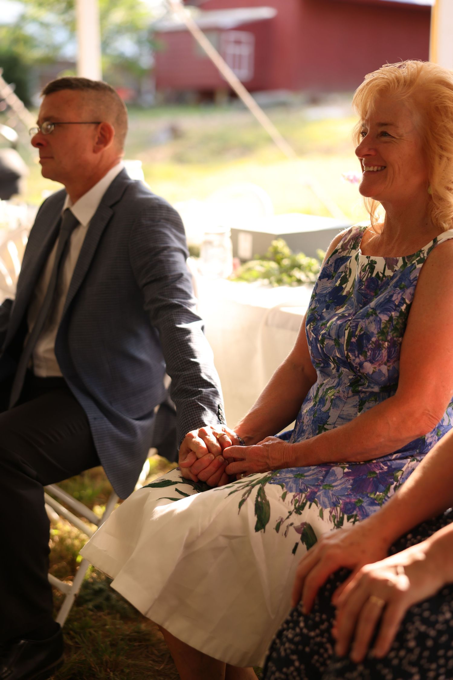Smiling woman in floral dress holding hands with man in suit at wedding ceremony.
