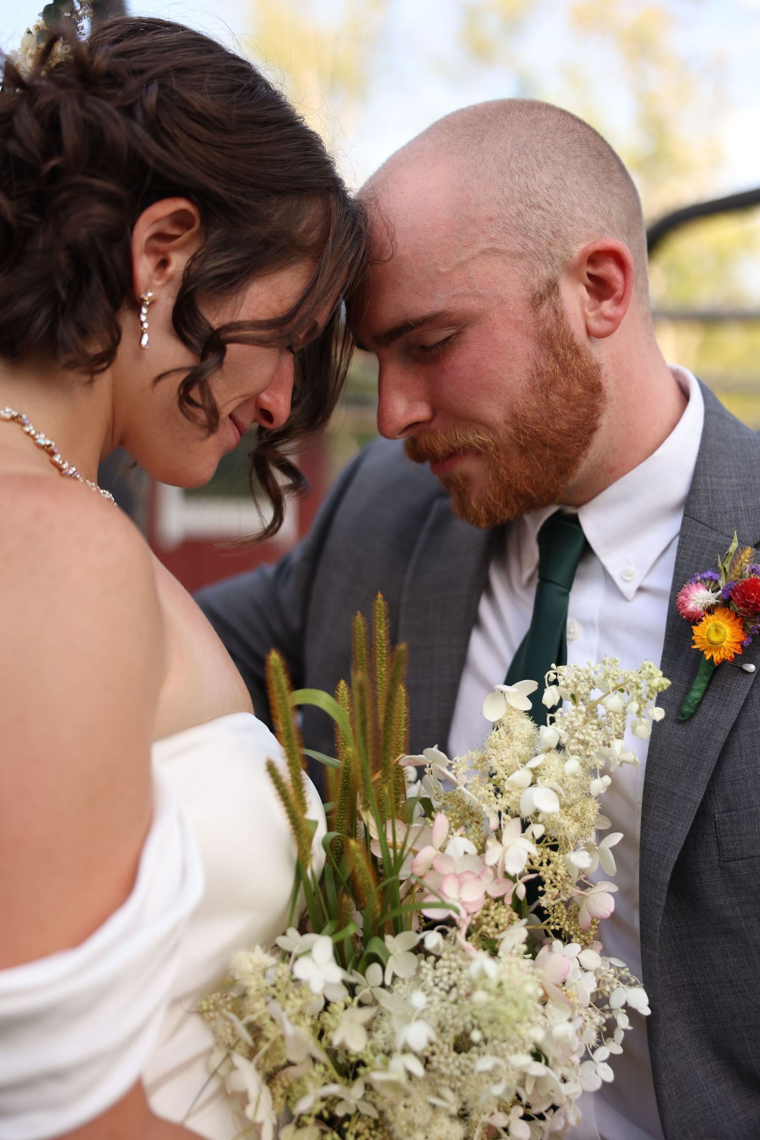 Bride and groom touching foreheads tenderly while holding a wildflower bouquet on their wedding day.