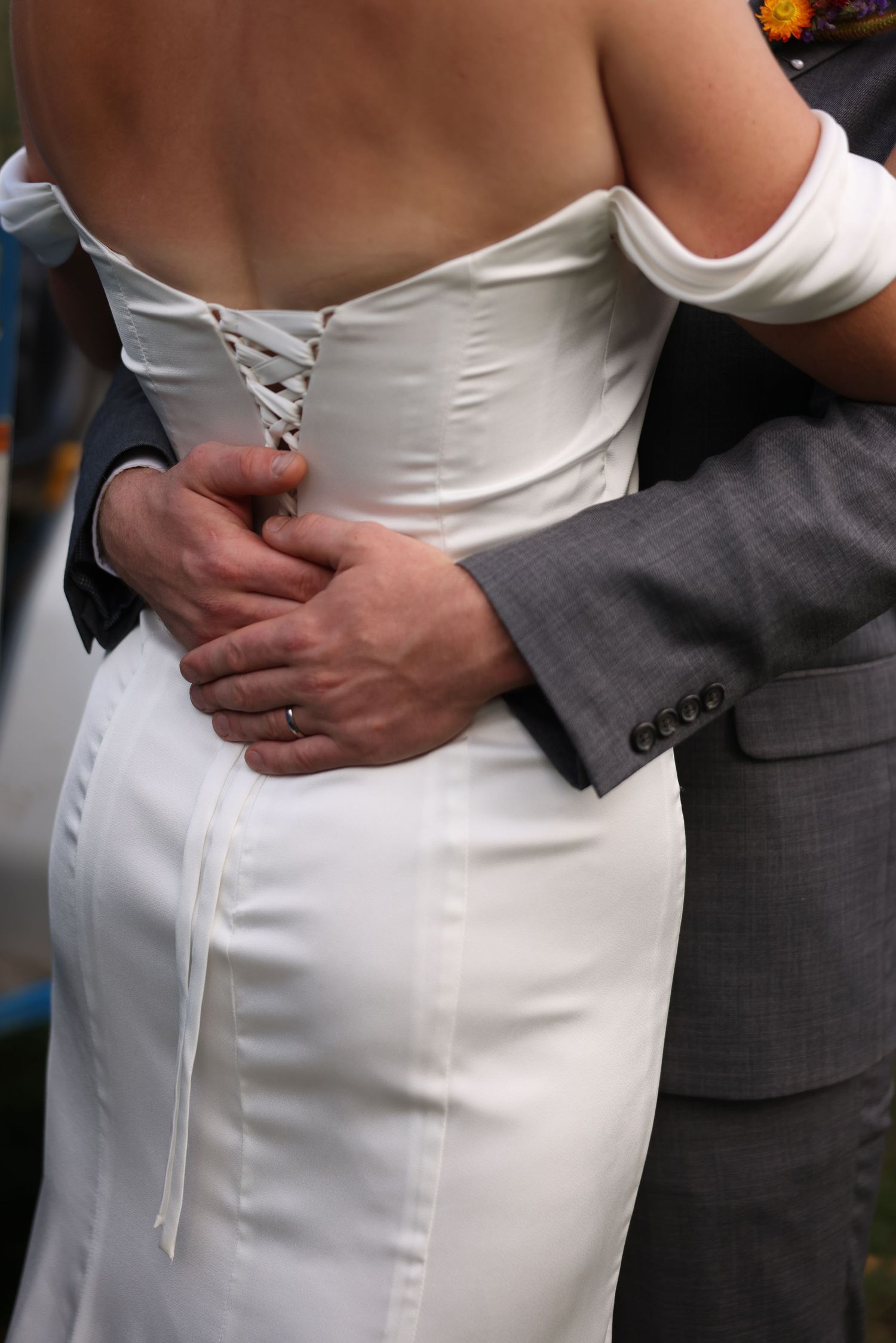 Close-up of groom's hands clasped around bride's white lace-back wedding gown waist.