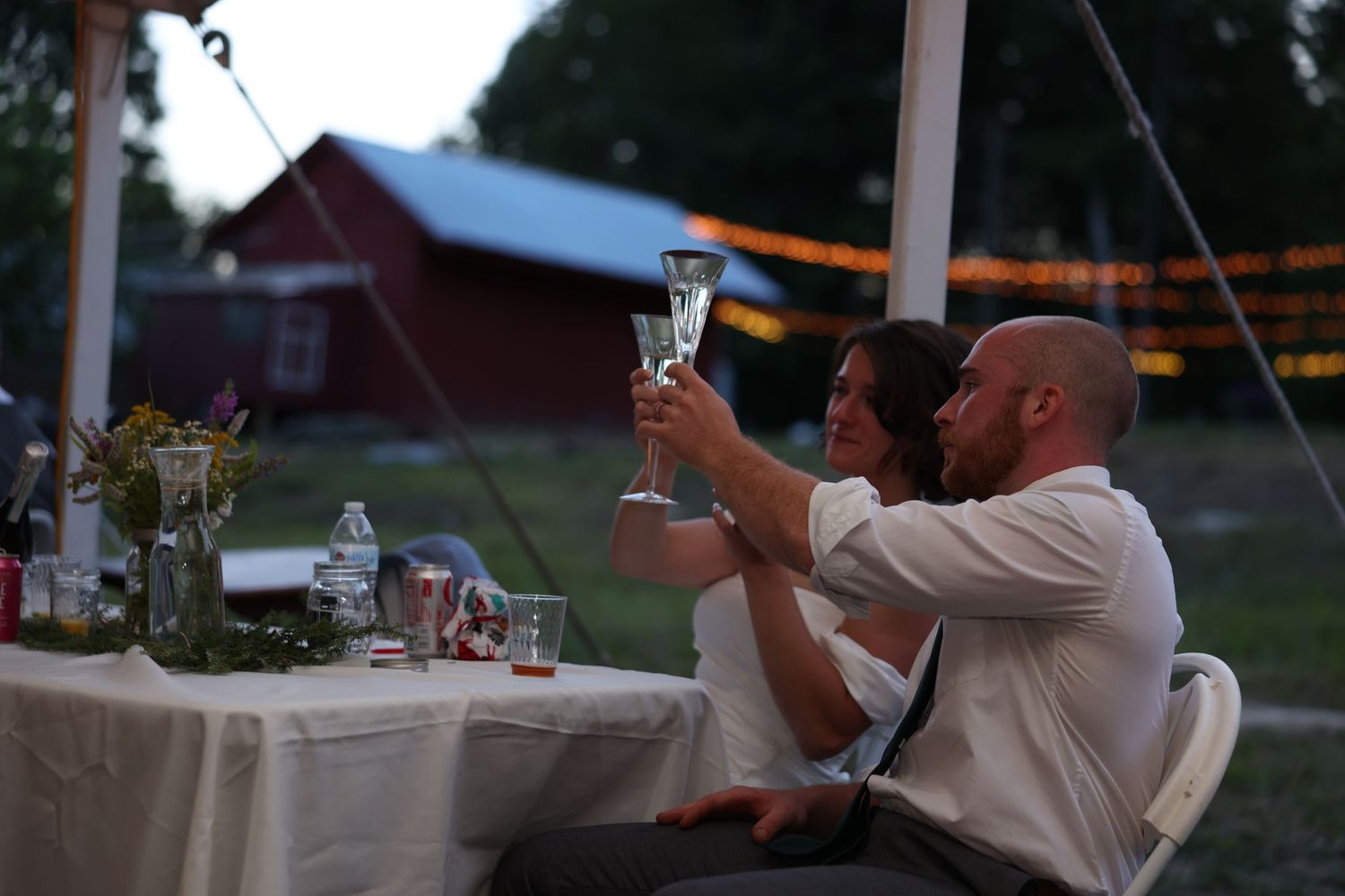 Newlyweds raise champagne glasses in a toast at their outdoor tented evening reception.