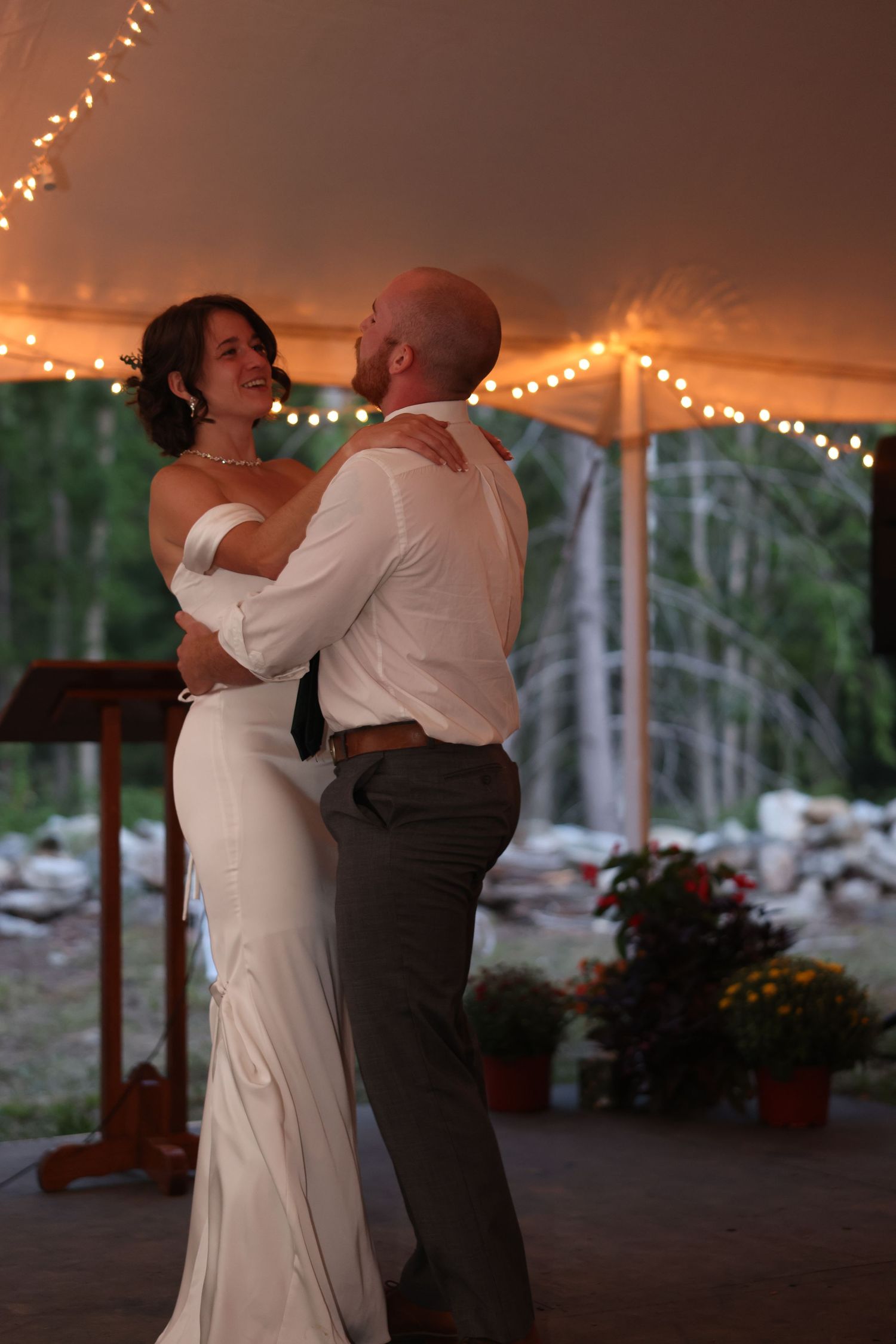 Bride and groom share their first dance under warm string lights in a romantic wedding tent.