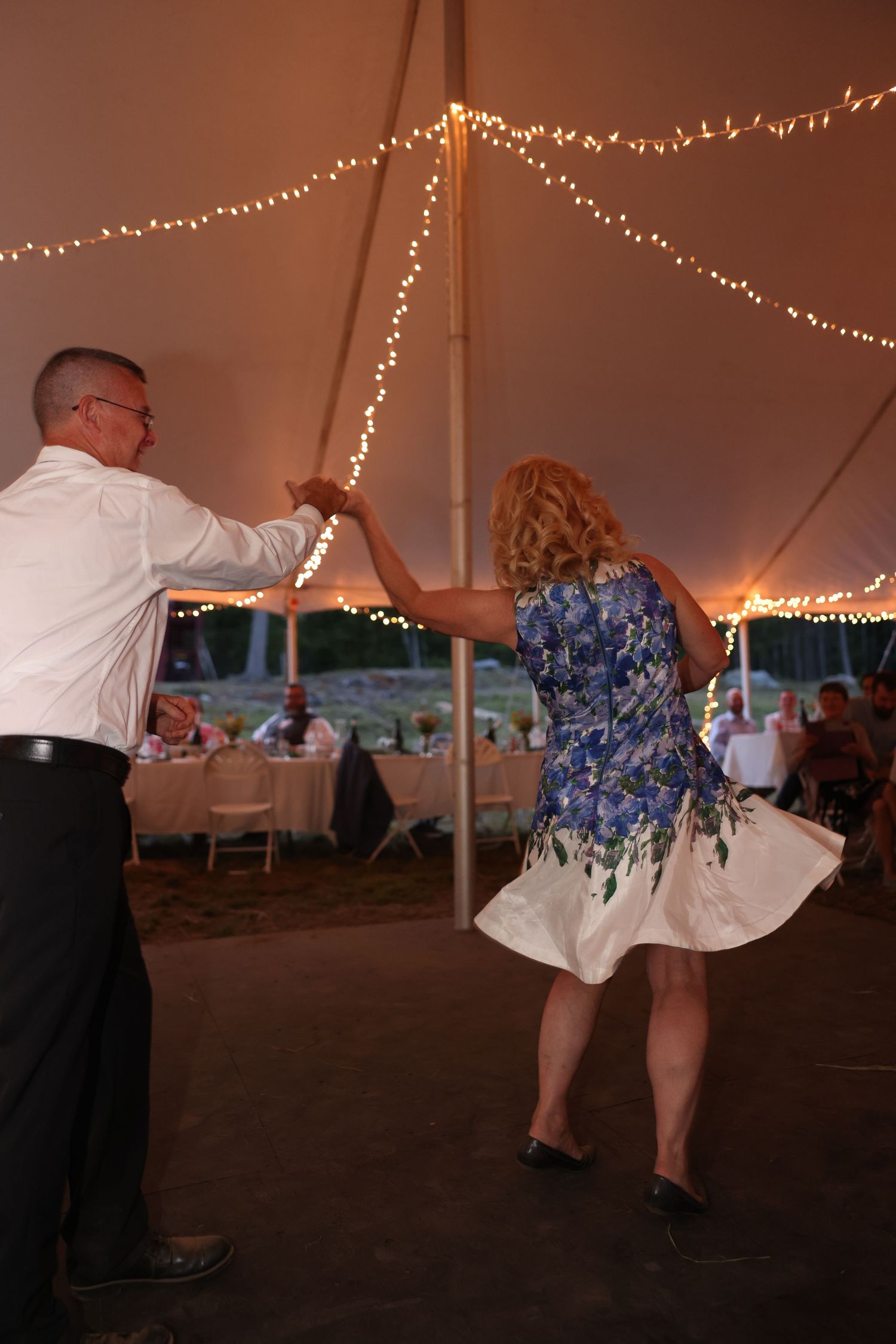 Couple energetically dancing under string lights at a warm evening wedding tent reception.