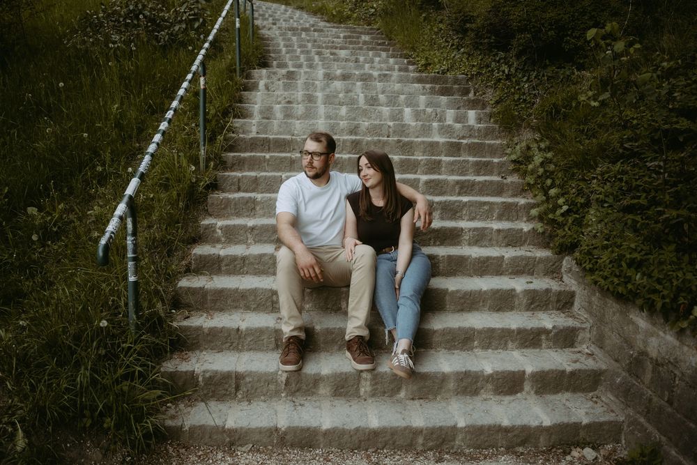 Couple sitting together on outdoor stone steps surrounded by lush greenery, sharing a relaxed moment.