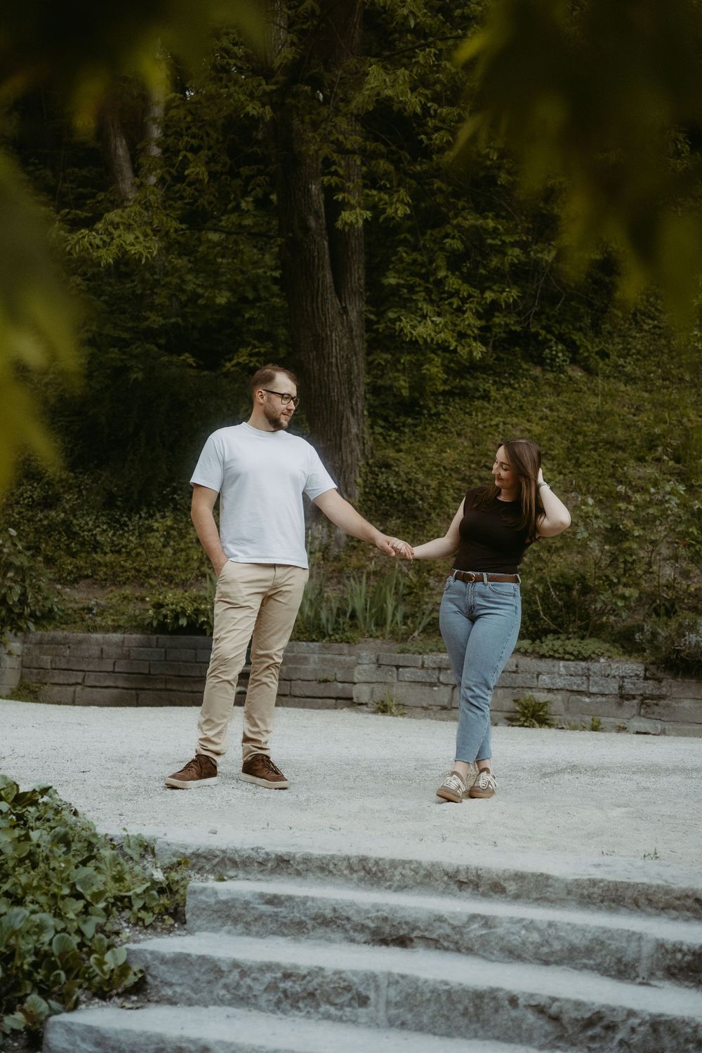 Couple holding hands and smiling while walking together in a lush green park on a sunny day.