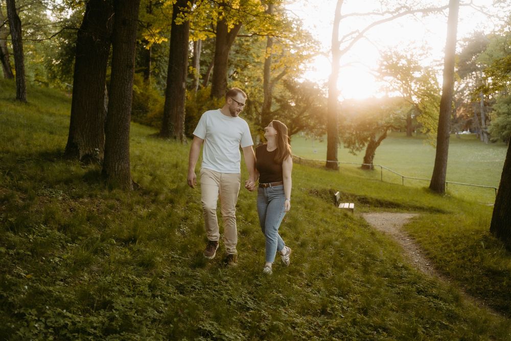 Couple walking hand in hand through a sunlit park with glowing golden hour light.