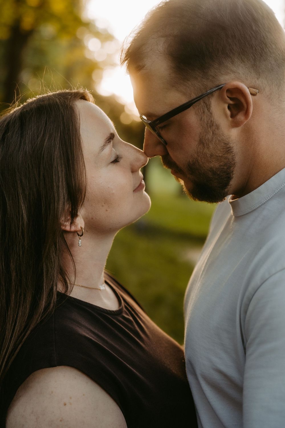 A romantic couple shares an intimate moment outdoors, nearly kissing in warm golden sunset light.