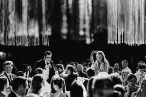 Wedding reception guests raise their hands in celebration during an indoor evening event.