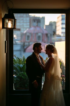 Silhouetted couple sharing intimate moment against cityscape window view at dusk.