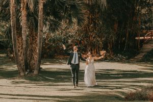 A romantic wedding ceremony takes place on a tree-lined path in a sunlit forest.