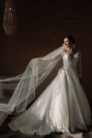 Elegant white wedding dress with lace details and flowing veil displayed against dark background.