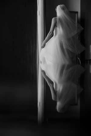 Artistic black and white silhouette of flowing wedding dress in doorway.