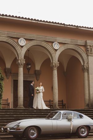 Classic vintage Jaguar E-Type convertible parked under Mediterranean-style arched colonnade.