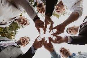 Circle of hands toasting with champagne glasses from below perspective.
