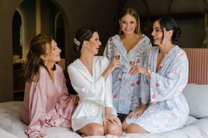 Wedding party members in pink robes and white loungewear relax together.