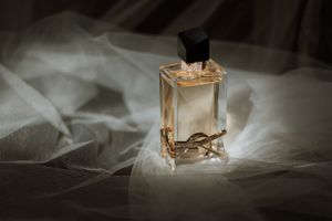 Elegant perfume bottle on white silk fabric with soft lighting and shadows.