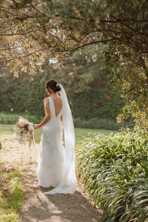 Elegant bridal portrait on a garden path with flowing veil and bouquet in golden afternoon light.