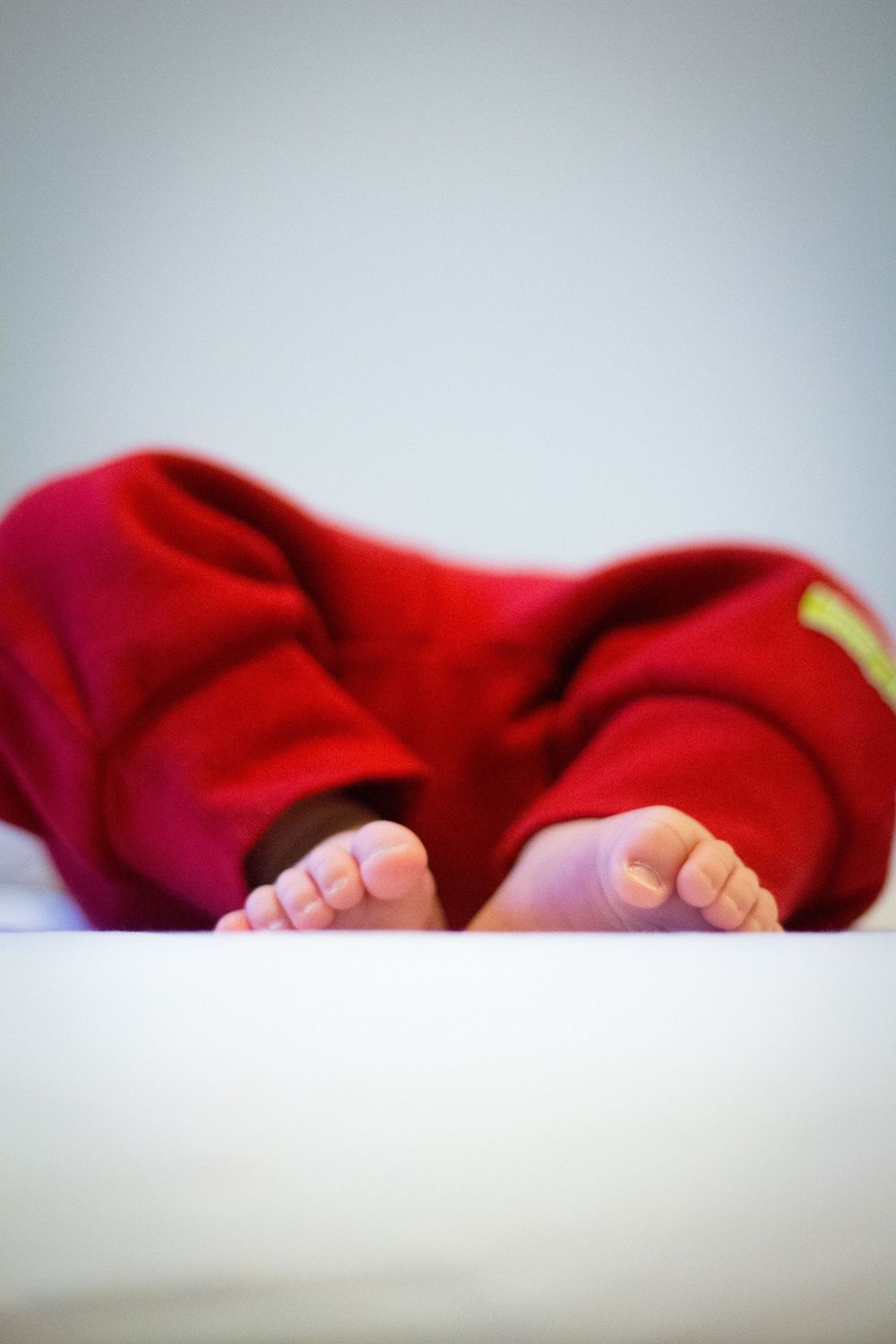 Newborn baby in a red outfit lying down with tiny feet visible at the edge of a white surface.