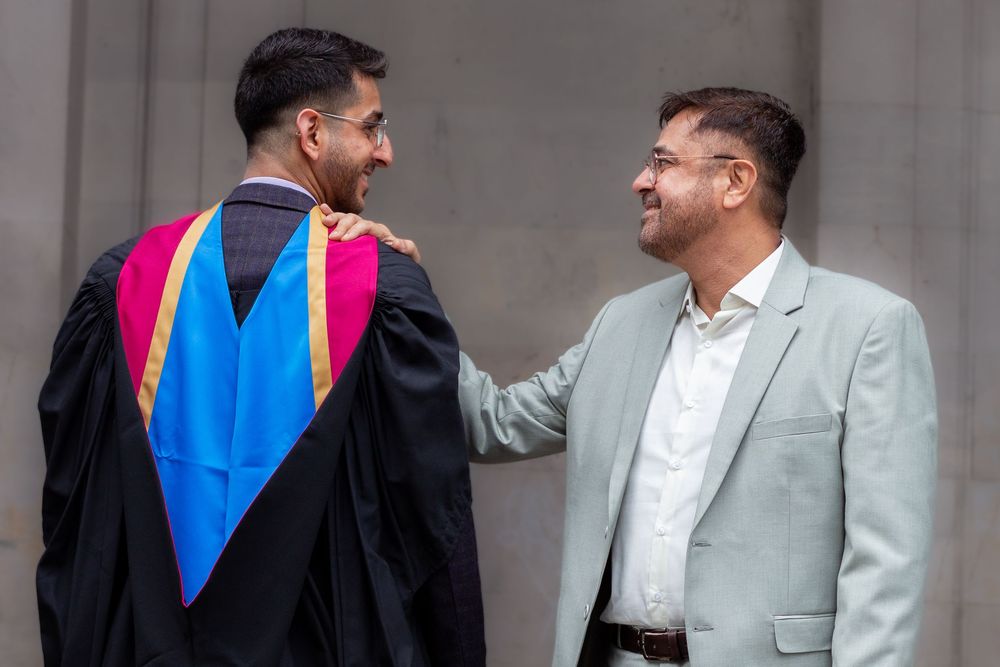 Graduate in academic gown shares proud moment with smiling Dad at graduation ceremony.