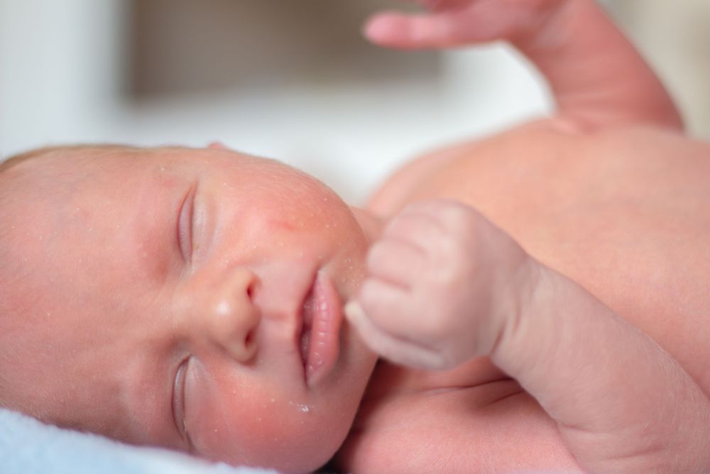 Close-up of a peaceful sleeping newborn baby with hand raised near face on white blanket.