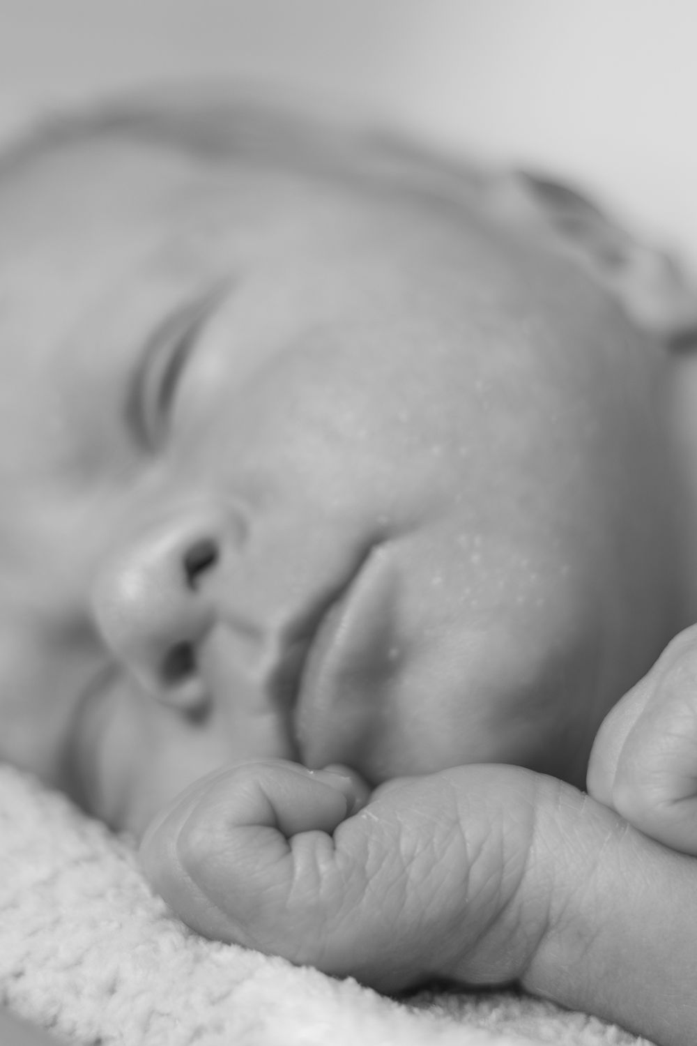 Black and white close-up of a sleeping newborn baby's face and clenched tiny fists.