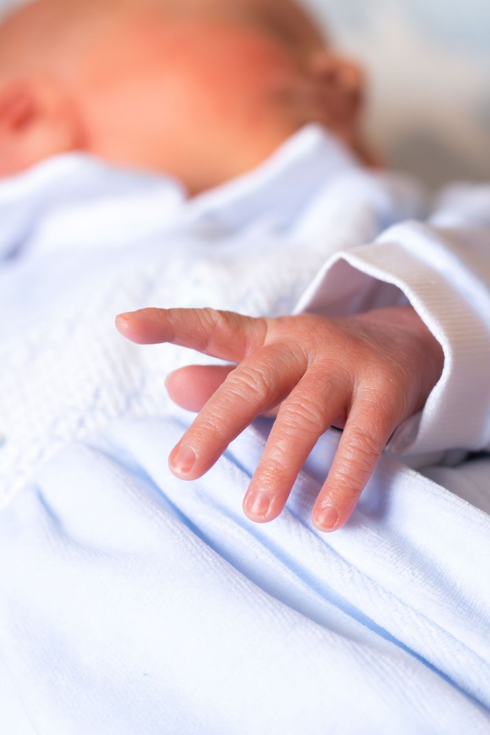Close-up of a sleeping newborn baby's tiny hand resting on a soft blue blanket.