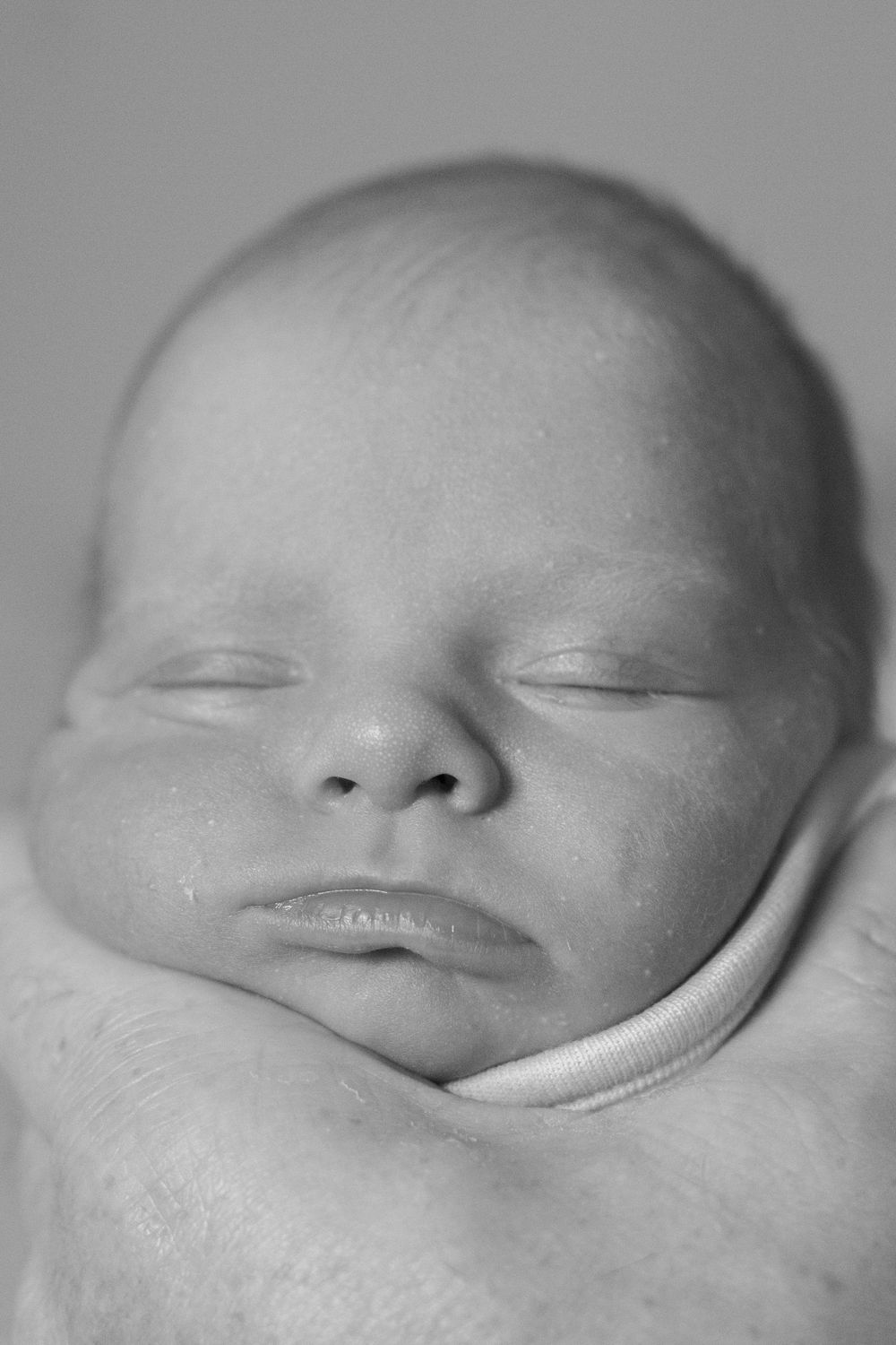 Black and white close-up portrait of a peaceful sleeping newborn baby's face.
