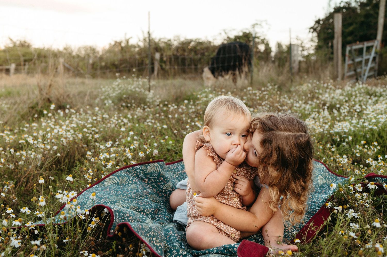 Toddler in floral romper walking barefoot on green grass with colorful berry bushes in background.