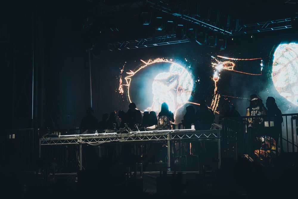 Dark concert stage with glowing circular light installations and silhouetted performers creating an ethereal atmosphere.