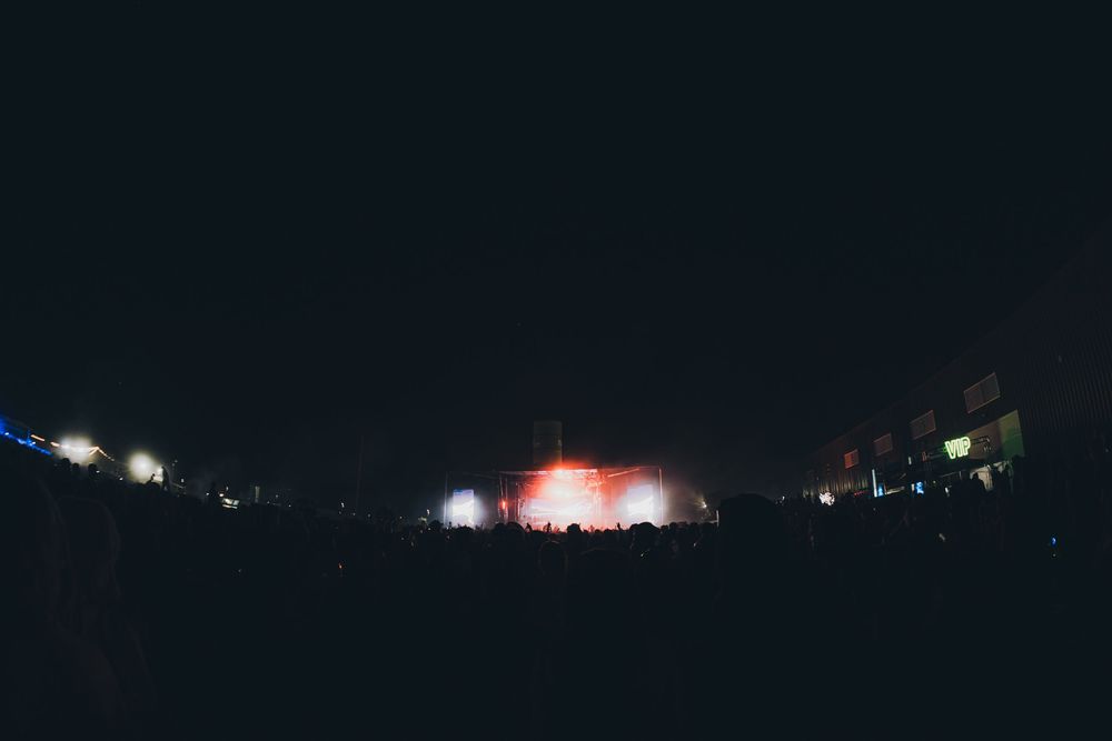 Crowd silhouette at night music festival with colorful red and white stage lights glowing in the dark.