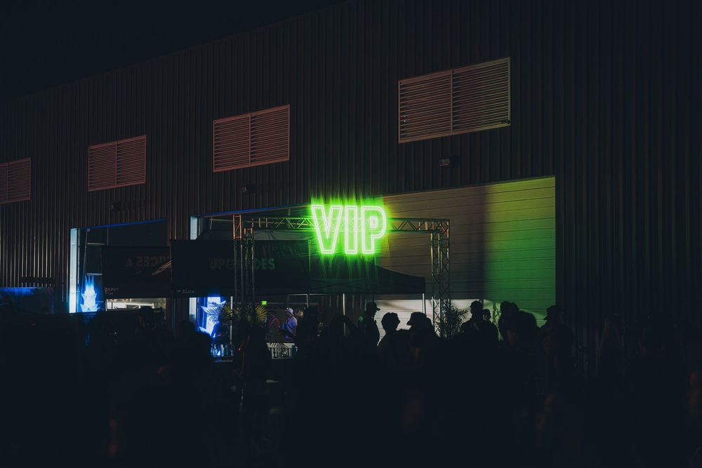 Neon green VIP sign glowing above a dark nightclub entrance with silhouetted crowd outside.