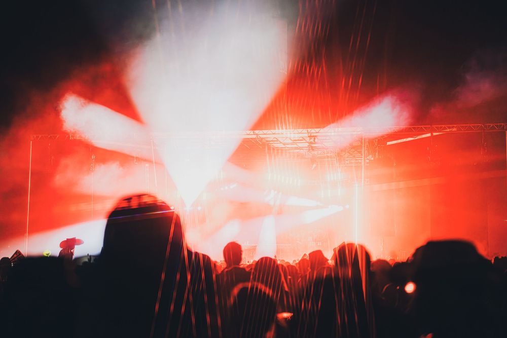 Crowd silhouettes at a concert with dramatic red and white laser light show on stage.