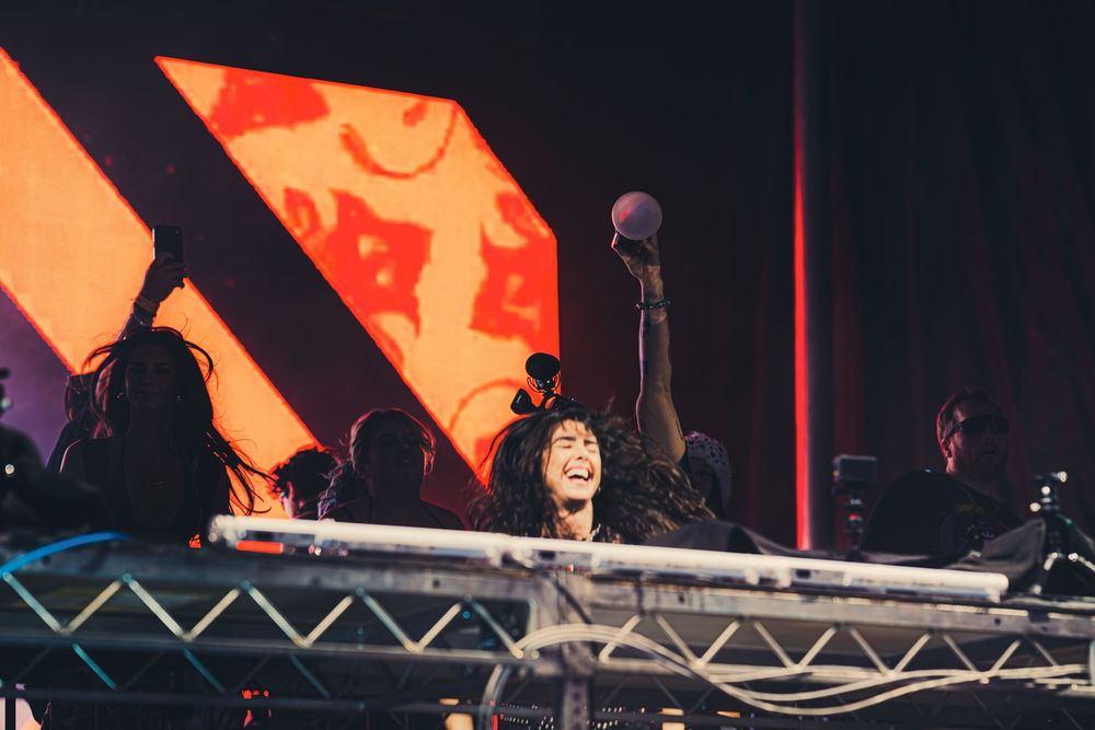 Female DJ performing on stage, raising microphone triumphantly under red stage lights at a live music event.