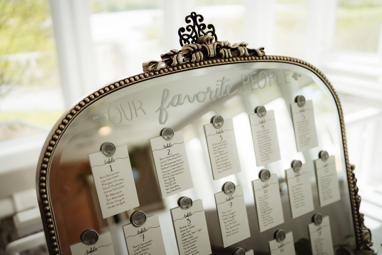 Elegant vintage mirror wedding seating chart displaying table assignments on small cards with decorative ornate gold frame.