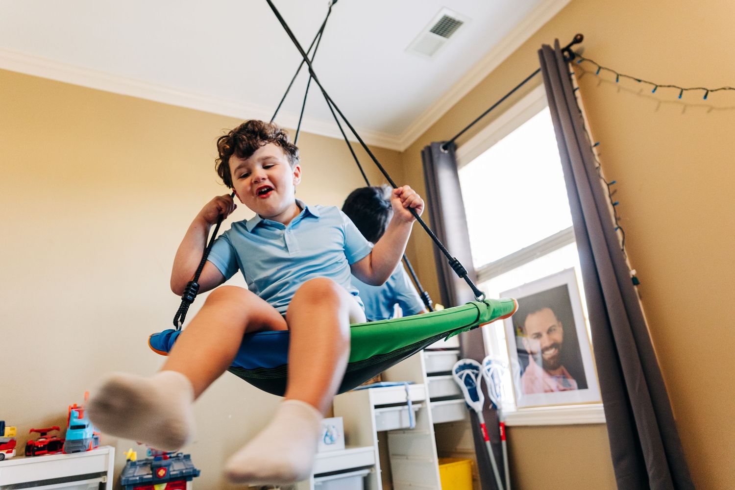 Happy boy swinging on indoor therapy swing in playroom, laughing with joy during sensory play activity at home.