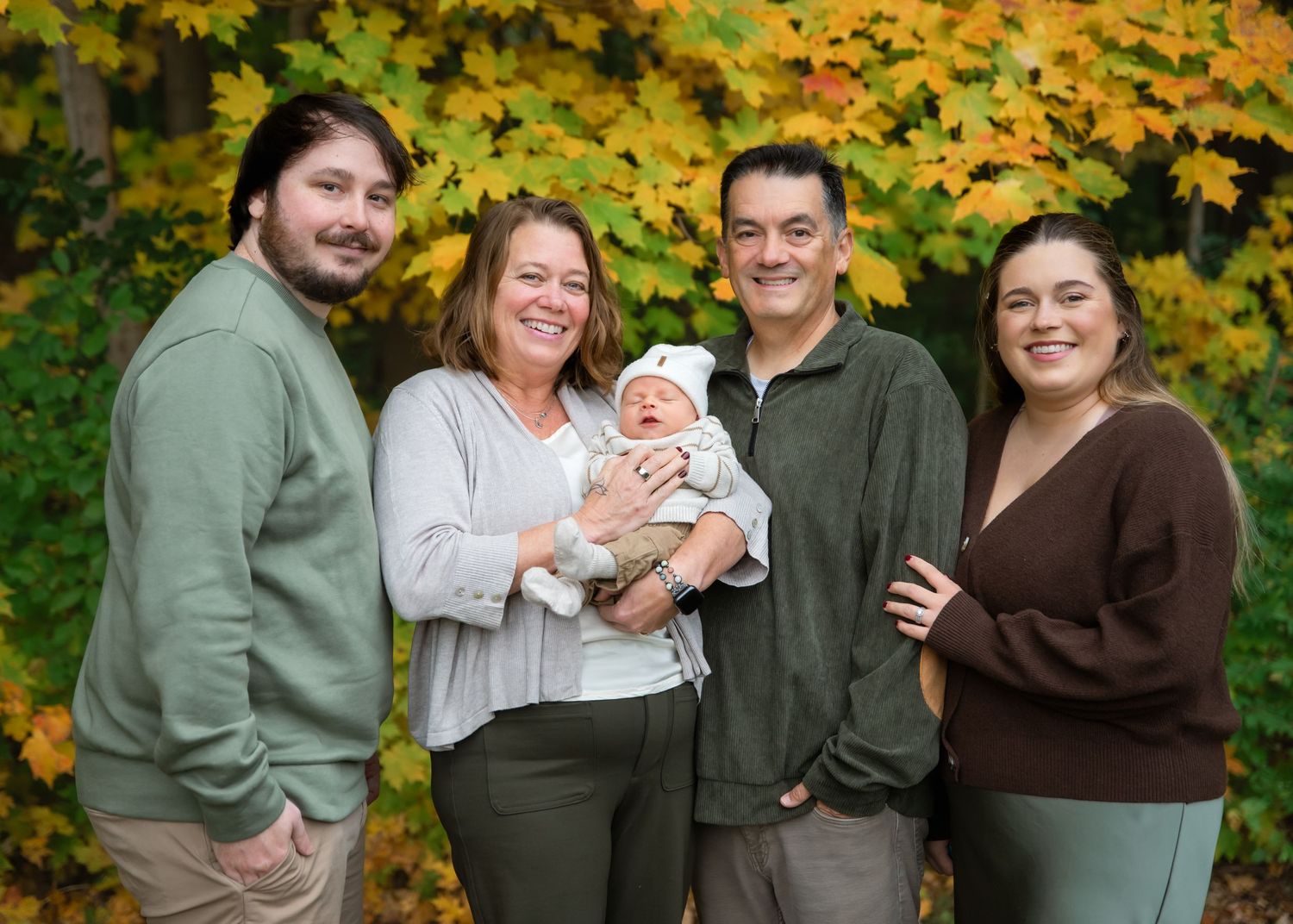 Family of five posing outdoors in autumn with vibrant yellow foliage, holding a newborn baby.
